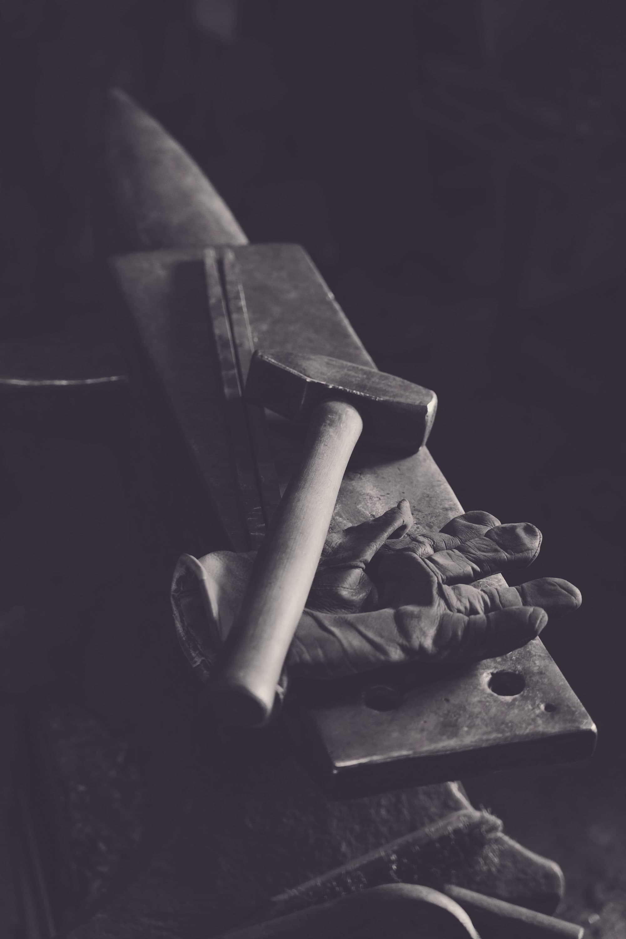 A blacksmith at the forge, hammer raised over glowing metal, sparks lifting from the anvil.