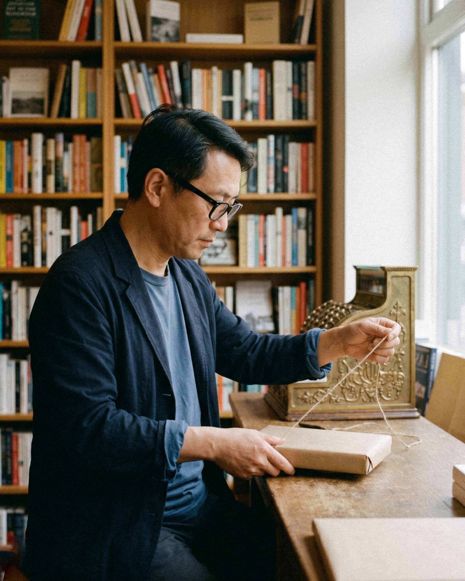 A bookseller wraps a book in brown paper behind the counter of an independent bookshop.